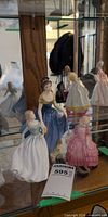 Front view of three Royal Doulton figurines in display cabinet