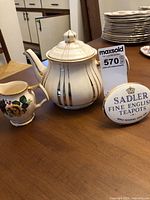 Teapot with lid and creamer displayed together beside Sadler sign