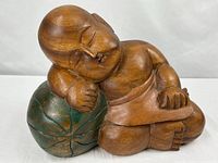 Front view of carved sleeping child figure leaning on green ball