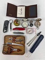 Overview of all items laid out including wallet, grooming kit, tools, paperweight, pill box, compasses