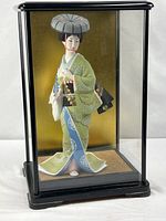 Full view of geisha doll inside black wood and glass case