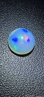 Round cabochon opal showing play-of-color on black background
