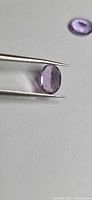 Amethyst in tweezers showing face-up view, another stone blurred in background