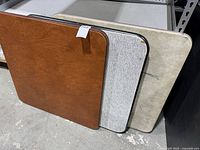 Three folding card tables stacked showing tops: brown woodgrain, grey, beige