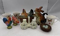 Group shot of all ceramics: rabbit teapot, hen dish, mugs, rooster shakers, chick motif shakers with caddy, nest