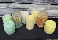 All eight candles grouped on black cloth; shows variety of flameless pillars and two jar candles