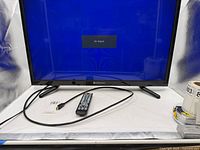 Television front view powered on with remote and power cord visible
