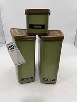 Three olive green metal canisters stacked, showing front labels flour, sugar, tea, and size reference tag
