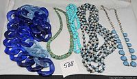 Overview of five necklaces laid flat including blue resin chain, turquoise heishi, turquoise round beads, marbled multi-strand beads, silver-tone Y-drop with blue stones