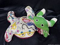 Front view of larger multicolour needlepoint frog pillow with smaller frog partially visible