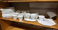 Stack of 15 snack plates, row of cups, creamer, sugar, small underplate, fan vase on wooden shelf