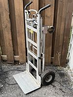 Front side view of aluminum Cosco hand truck showing frame, toe plate, wheels, strap and handles