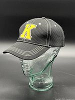 Front three-quarter view of black cap showing yellow "K" logo and texture