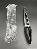 Tong removed from plastic sleeve showing stainless steel body and black silicone tips