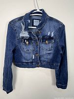 Front view of cropped distressed blue denim jacket on hanger