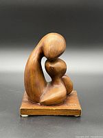 Front view of solid wood abstract sculpture of parent embracing child on wooden base