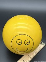 Full view of yellow EPCO bowling ball with smiley face and ruler for scale