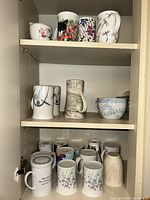 Cabinet shelves showing full assortment of mugs and soup cup
