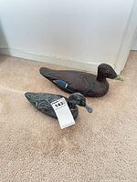 Both wooden duck decoys side by side on carpet