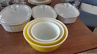 Front view of three CorningWare oval casseroles with lids and three nested Pyrex yellow bowls