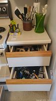 Two open drawers showing flatware and mixed utensils beside stove
