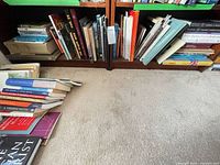 Books on two-shelf bookcase with additional stack on floor