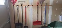 Long-handled garden and snow tools hanging on garage wall