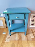 Front view of teal nightstand showing drawer, knob, open shelf