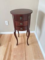 Front view of round side table showing three drawers and cabriole legs