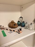 Shelf view showing brown lidded dish, cow-pattern spoon rest, clear glass salt and pepper shakers