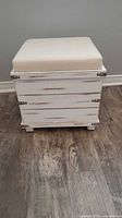Front view of white distressed storage ottoman cube with beige cushion