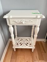 front view of white ornate side table showing drawer and shelf