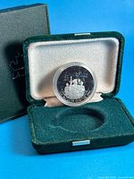 Open green velvet case showing coin in capsule, outer box behind