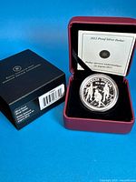 Coin in capsule inside presentation case with certificate, outer box nearby