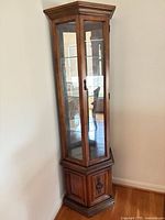 Full view of corner curio cabinet showing wood finish, glass door, and lower base