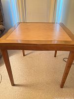 Front view of square wood game table showing leather inset top and tapered legs