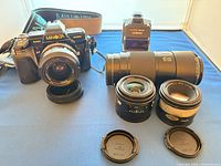 Camera body front view with mounted lens and strap, lenses and flash arranged on blue surface