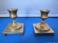 Pair of brass candlestick holders, side angle showing square bases and patina