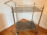Full view of gold-tone metal tea trolley showing two smoked glass shelves and casters