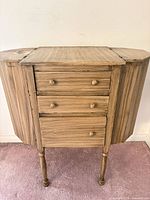 Front view of wooden sewing cabinet showing three drawers and turned legs