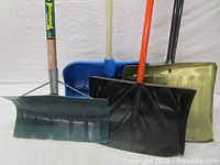 Front view showing four shovel blades: green metal, black plastic, gold metal, blue plastic