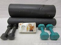 Group shot showing two rolled mats, skip rope box, teal dumbbells, black dumbbells