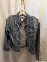 Front view of blue denim jacket on hanger