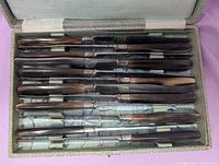 Open box showing 12 knives with faux horn handles and satin lining