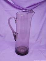 Full view of tall purple glass pitcher with handle and flared spout
