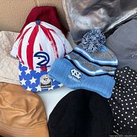 Stack including Hawks snapback, Tar Heels beanie, brown bucket, silver hat, polka dot bucket