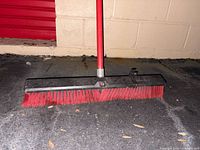 Close-up of broom head showing thick red bristles and metal block