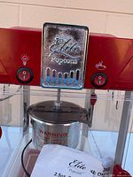 Front view showing Elite Popcorn plate, control switches, stainless kettle and instruction sheet inside cabinet