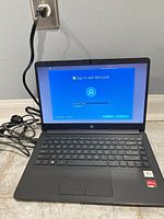 Laptop open, powered on showing Windows setup screen, AC adapter connected