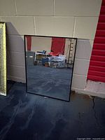 Front view of rectangular black framed mirror leaning against wall